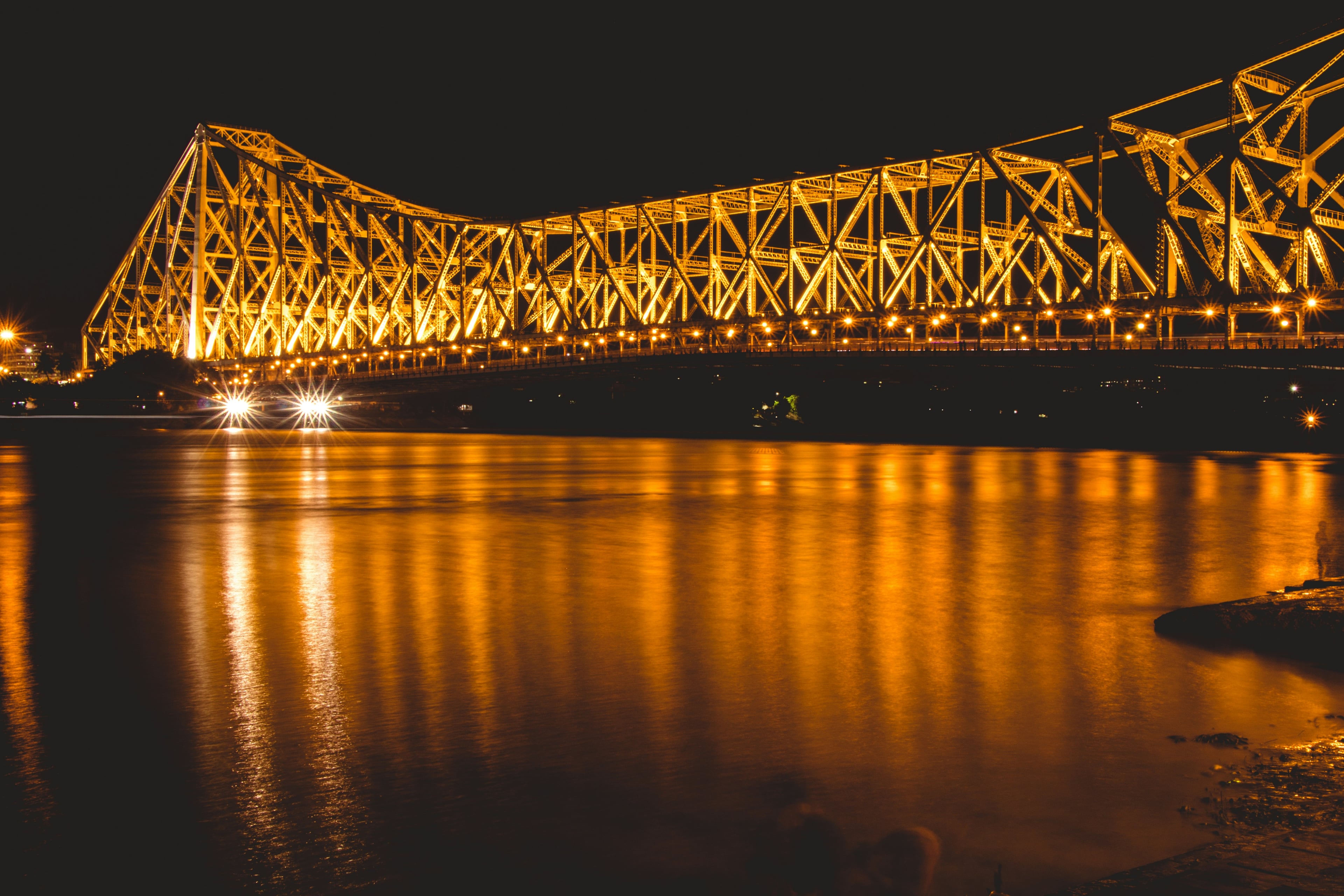 Howrah Bridge lit up in gold at night over the Hooghly river